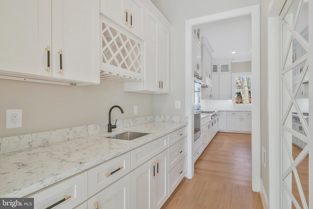 kitchen featuring stainless steel gas stovetop, light hardwood / wood-style floors, sink, white cabinets, and light stone counters