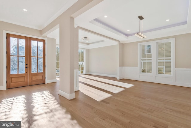 foyer entrance featuring crown molding, french doors, light hardwood / wood-style flooring, an inviting chandelier, and a tray ceiling