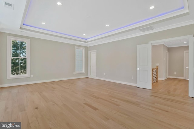 empty room with crown molding, light hardwood / wood-style flooring, and a tray ceiling