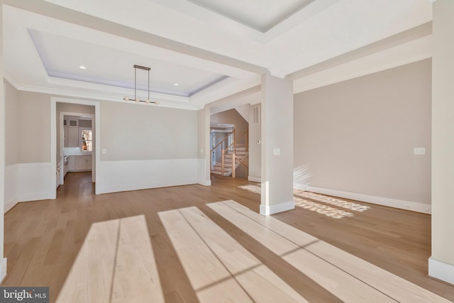 empty room with light wood-type flooring, a chandelier, and a tray ceiling