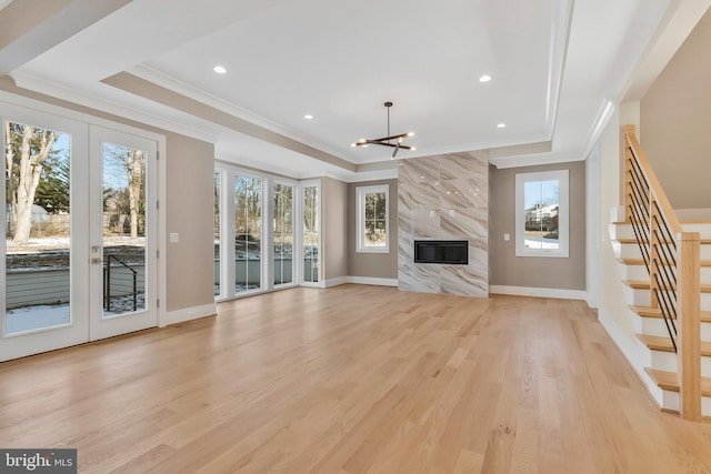 unfurnished living room featuring a fireplace, light hardwood / wood-style floors, a tray ceiling, and french doors