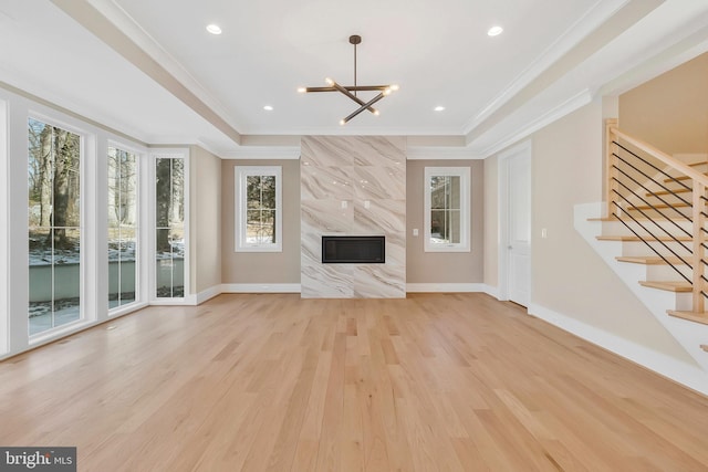 unfurnished living room with crown molding, light wood-type flooring, a high end fireplace, and an inviting chandelier