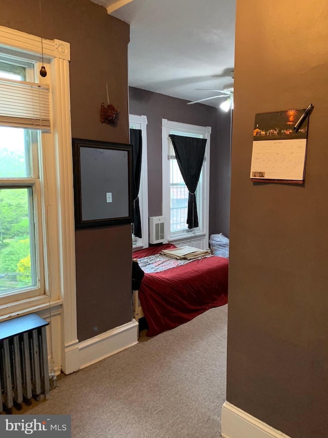 carpeted bedroom with ceiling fan, multiple windows, and radiator