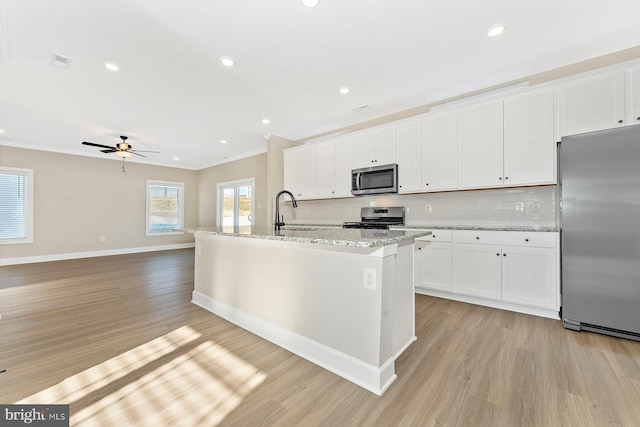 kitchen featuring appliances with stainless steel finishes, decorative backsplash, white cabinets, sink, and an island with sink