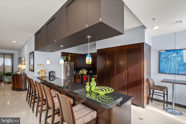 kitchen featuring pendant lighting, a kitchen breakfast bar, stainless steel fridge, kitchen peninsula, and dark brown cabinets