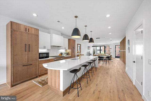 kitchen with a spacious island, decorative light fixtures, premium range hood, white cabinets, and sink