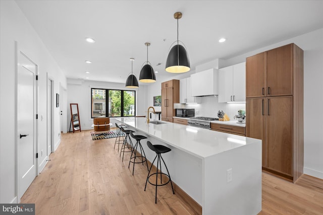 kitchen with white cabinets, decorative light fixtures, wall chimney range hood, an island with sink, and sink