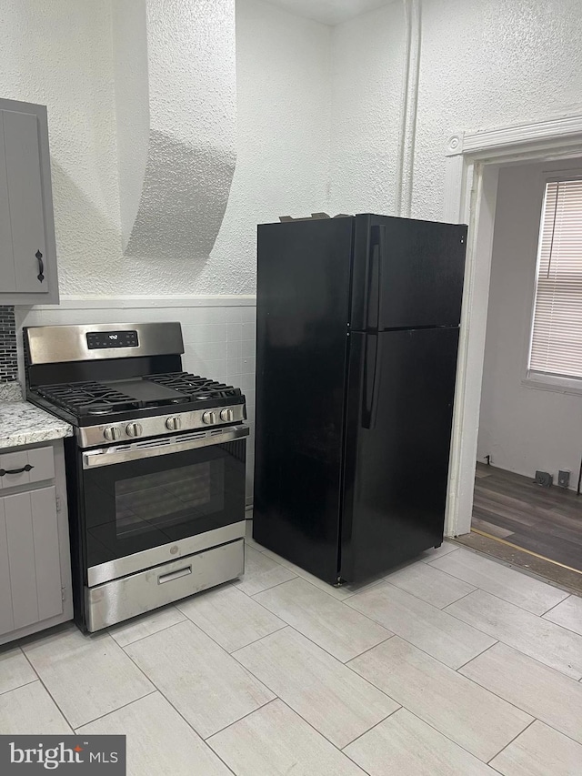 kitchen featuring gray cabinets, black refrigerator, and stainless steel gas range