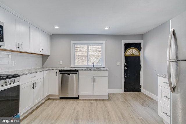 kitchen with tasteful backsplash, white cabinetry, stainless steel appliances, light stone countertops, and light wood-type flooring