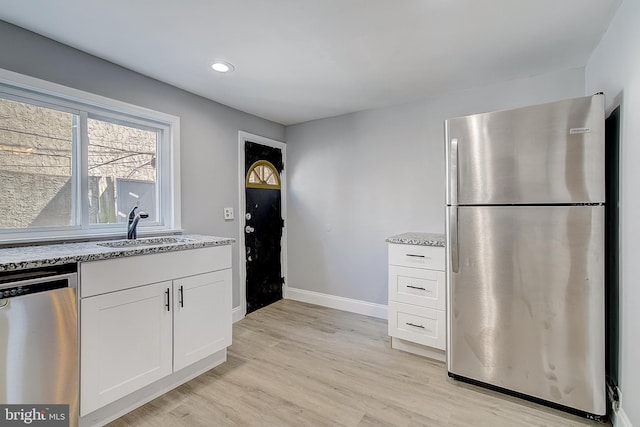 kitchen with white cabinetry, sink, light stone counters, stainless steel appliances, and light hardwood / wood-style flooring