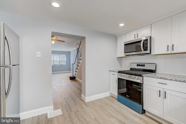 kitchen featuring light hardwood / wood-style flooring, appliances with stainless steel finishes, white cabinetry, backsplash, and light stone countertops