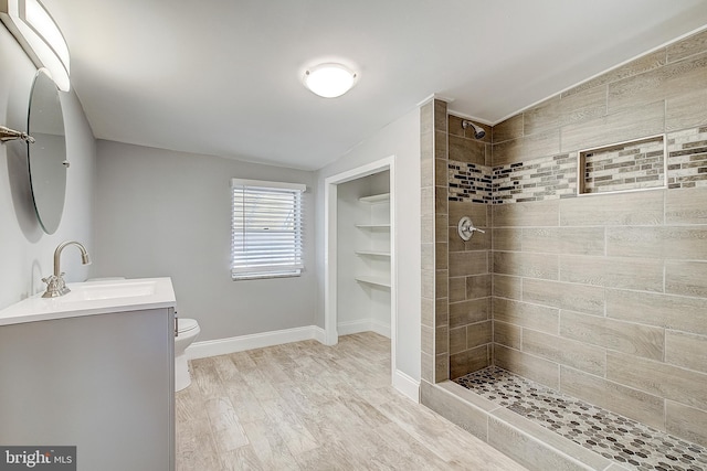 bathroom with vanity, a tile shower, wood-type flooring, vaulted ceiling, and toilet