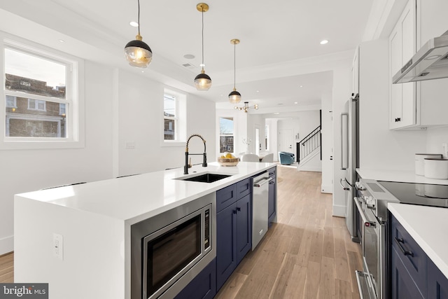 kitchen featuring a kitchen island with sink, sink, white cabinets, decorative light fixtures, and stainless steel appliances