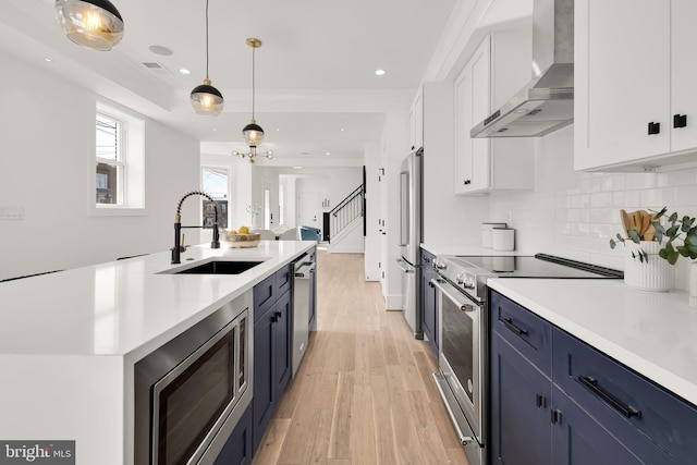 kitchen with wall chimney exhaust hood, sink, white cabinets, blue cabinets, and stainless steel appliances