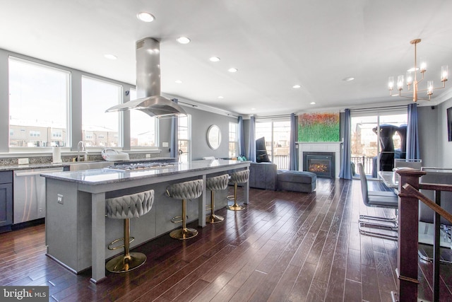 kitchen with light stone countertops, island exhaust hood, hanging light fixtures, a kitchen island, and stainless steel appliances