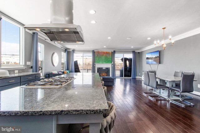 kitchen featuring decorative light fixtures, dark hardwood / wood-style flooring, island range hood, ornamental molding, and stainless steel gas stovetop