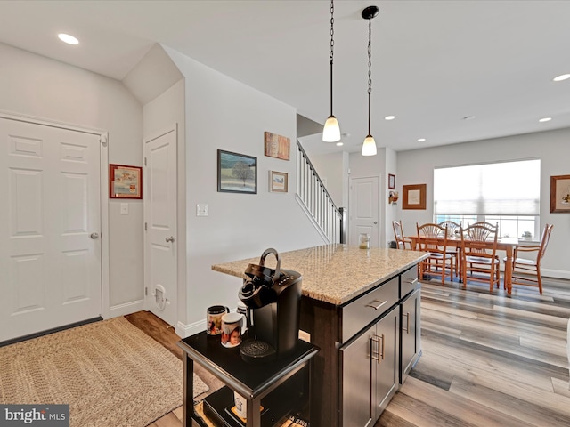 kitchen featuring dark brown cabinets, decorative light fixtures, light stone countertops, a center island, and light hardwood / wood-style floors