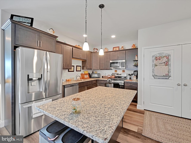 kitchen featuring hanging light fixtures, appliances with stainless steel finishes, a kitchen island, light hardwood / wood-style floors, and a breakfast bar area