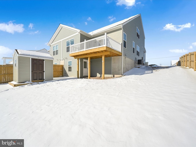 snow covered back of property featuring a wooden deck and a shed