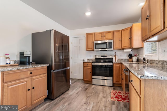 kitchen with sink, stainless steel appliances, light stone counters, tasteful backsplash, and light hardwood / wood-style floors