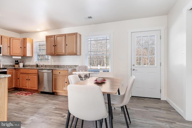 kitchen with stainless steel appliances, tasteful backsplash, light stone counters, light hardwood / wood-style floors, and light brown cabinetry