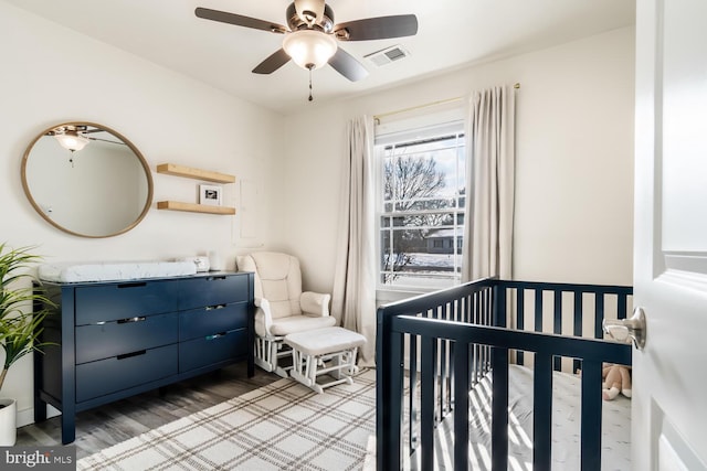 bedroom with a nursery area, hardwood / wood-style floors, and ceiling fan