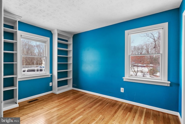 unfurnished room with built in features, light hardwood / wood-style floors, and a textured ceiling