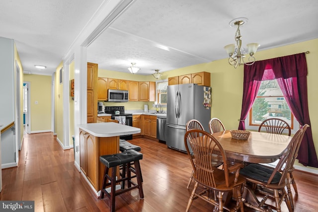 kitchen featuring wood-type flooring, a textured ceiling, a kitchen island, a chandelier, and stainless steel appliances