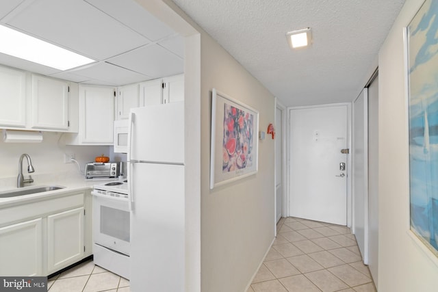 kitchen with white appliances, a textured ceiling, white cabinetry, sink, and light tile patterned flooring