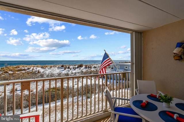 snow covered back of property with a water view and a view of the beach