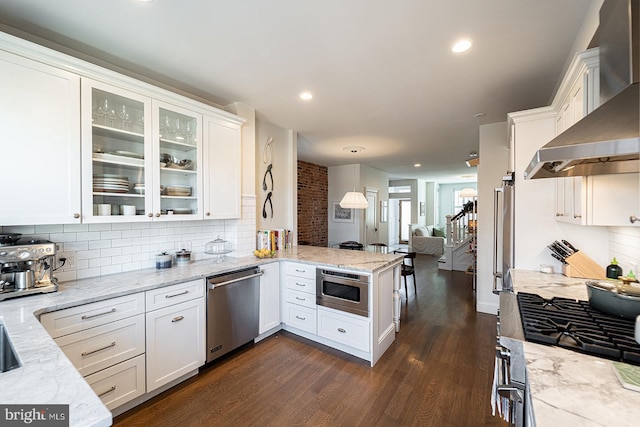 kitchen featuring wall chimney exhaust hood, light stone counters, appliances with stainless steel finishes, dark hardwood / wood-style flooring, and white cabinets