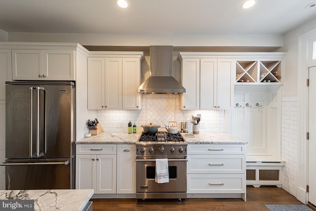 kitchen with white cabinets, dark hardwood / wood-style flooring, high end appliances, light stone counters, and wall chimney exhaust hood