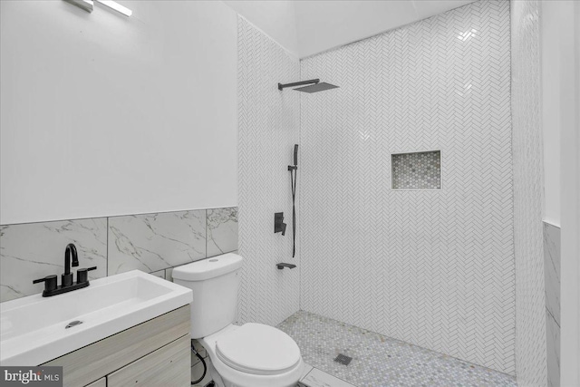 bathroom with vanity, toilet, tile walls, and tiled shower