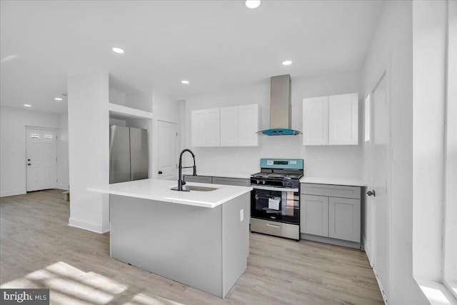 kitchen featuring appliances with stainless steel finishes, wall chimney range hood, white cabinets, sink, and an island with sink