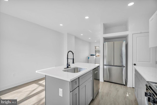 kitchen featuring appliances with stainless steel finishes, sink, washer / clothes dryer, gray cabinets, and an island with sink