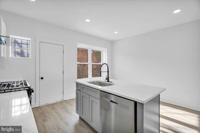 kitchen featuring gray cabinetry, sink, stainless steel dishwasher, light hardwood / wood-style flooring, and a center island with sink