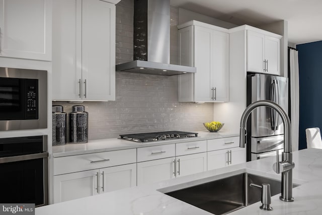 kitchen with appliances with stainless steel finishes, backsplash, white cabinetry, light stone countertops, and wall chimney range hood