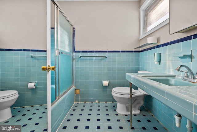 bathroom with tile patterned floors, toilet, bath / shower combo with glass door, and tile walls