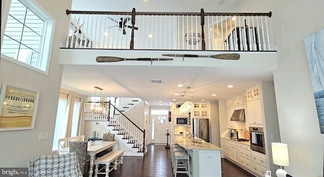 kitchen with light stone countertops, wall chimney exhaust hood, white cabinetry, stainless steel appliances, and hanging light fixtures