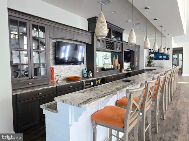 bar with backsplash, light stone countertops, pendant lighting, and dark hardwood / wood-style floors