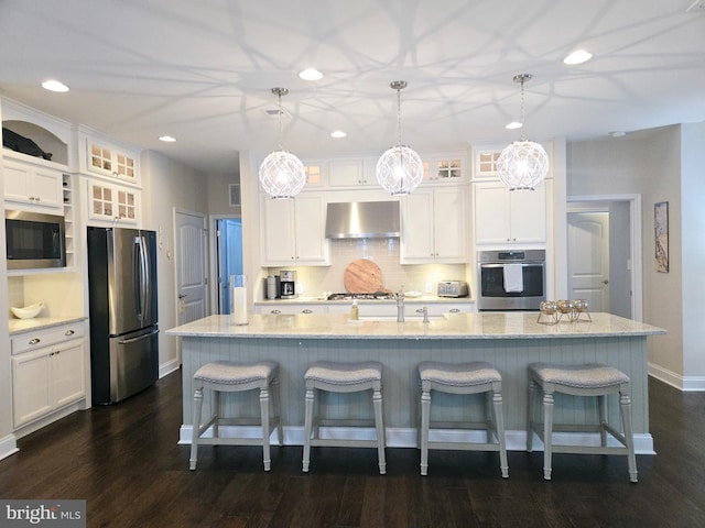 kitchen featuring hanging light fixtures, ventilation hood, stainless steel appliances, and a kitchen island with sink