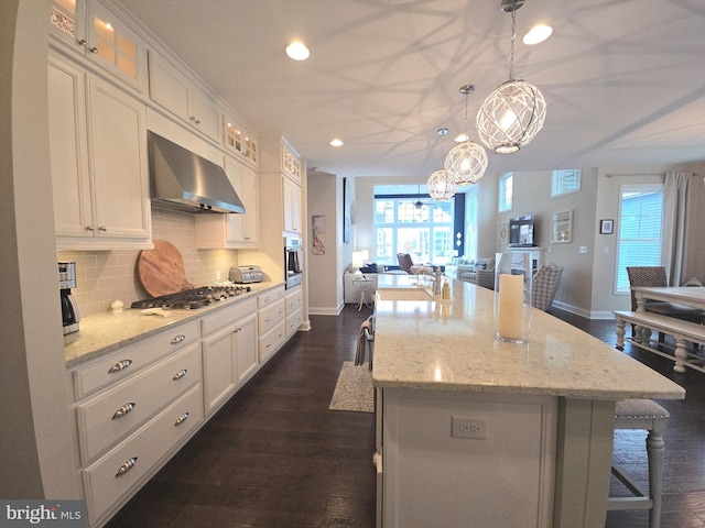 kitchen with a kitchen island with sink, a breakfast bar, wall chimney range hood, backsplash, and stainless steel appliances