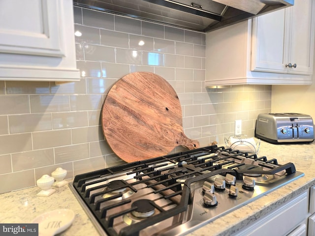 interior details featuring light stone counters, white cabinetry, decorative backsplash, and stainless steel gas stovetop