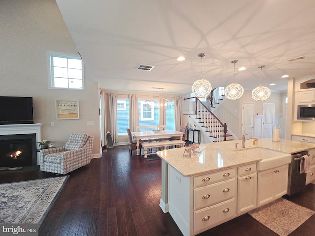 kitchen featuring hanging light fixtures, sink, white cabinets, light stone counters, and a kitchen island with sink