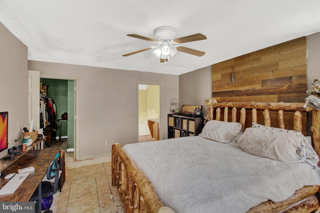 bedroom with ceiling fan, a walk in closet, connected bathroom, and wood walls