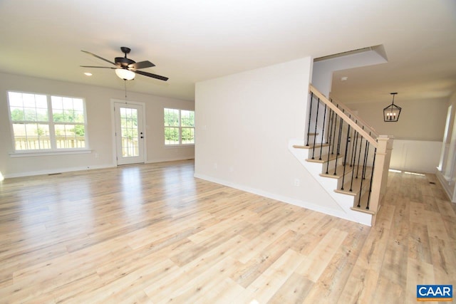 unfurnished living room featuring ceiling fan with notable chandelier and light hardwood / wood-style flooring