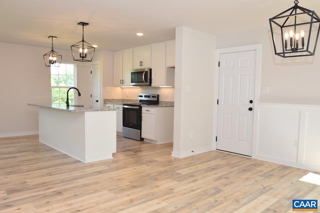 kitchen featuring white cabinets, a center island with sink, appliances with stainless steel finishes, and pendant lighting