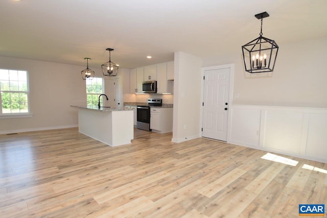 kitchen with appliances with stainless steel finishes, white cabinetry, light hardwood / wood-style floors, hanging light fixtures, and a center island with sink