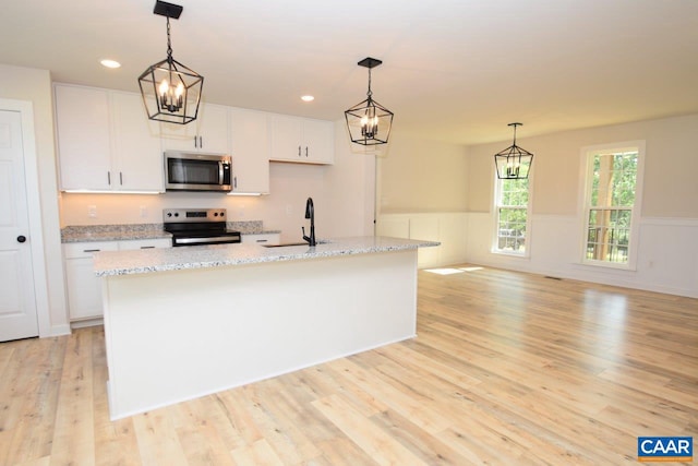 kitchen featuring appliances with stainless steel finishes, decorative light fixtures, white cabinetry, sink, and a center island with sink