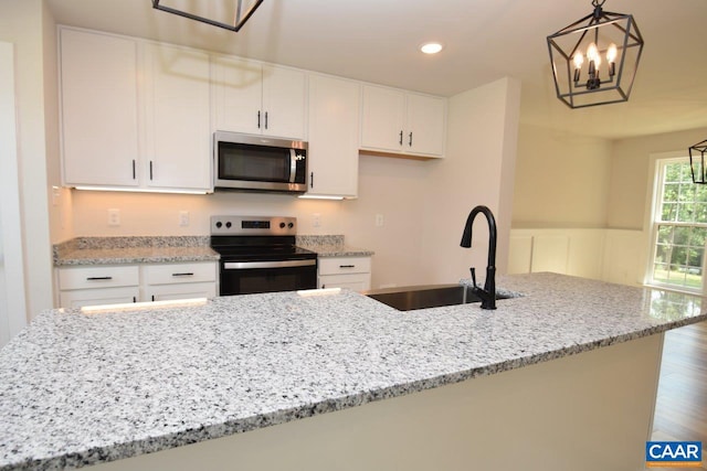 kitchen with pendant lighting, range with electric stovetop, sink, white cabinetry, and light stone counters